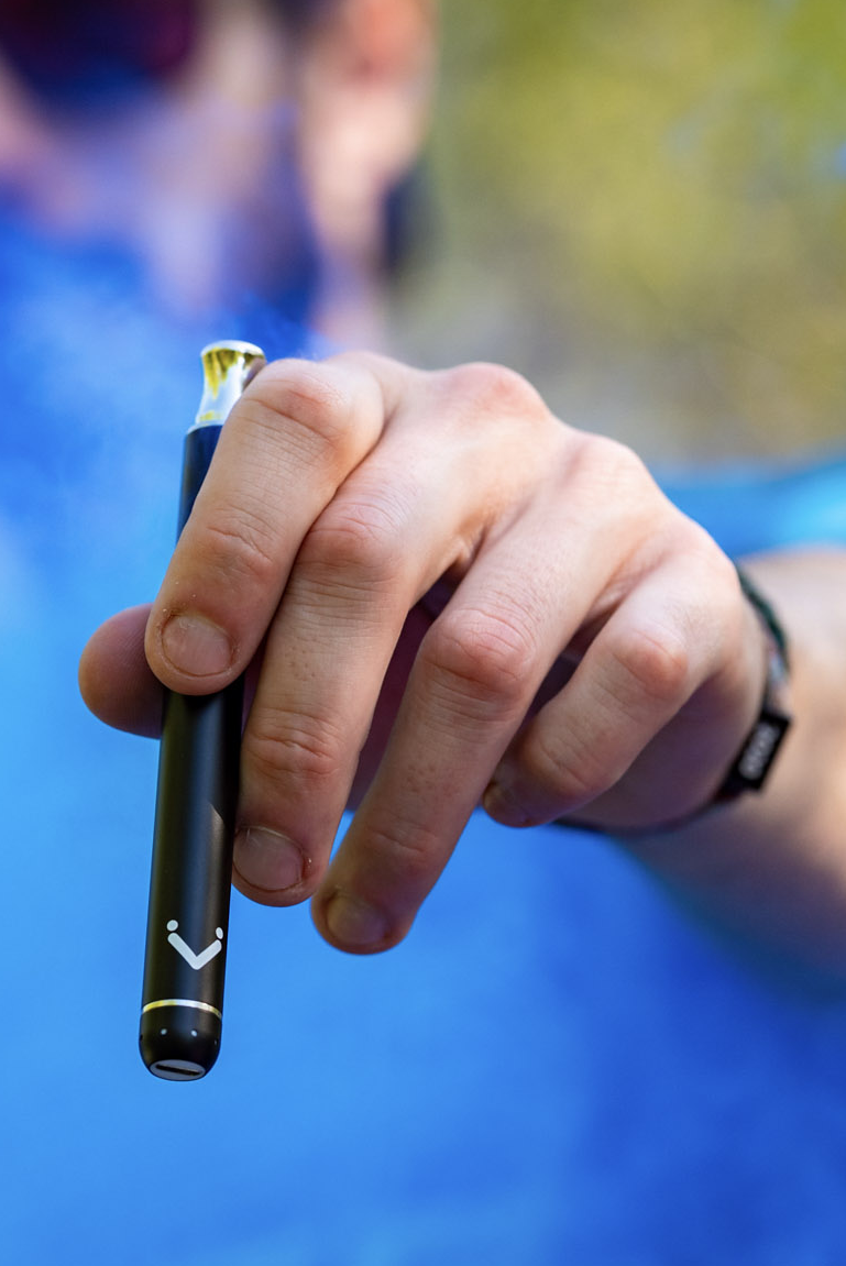 Hand holding a black Vuber battery with blue vapor behind it