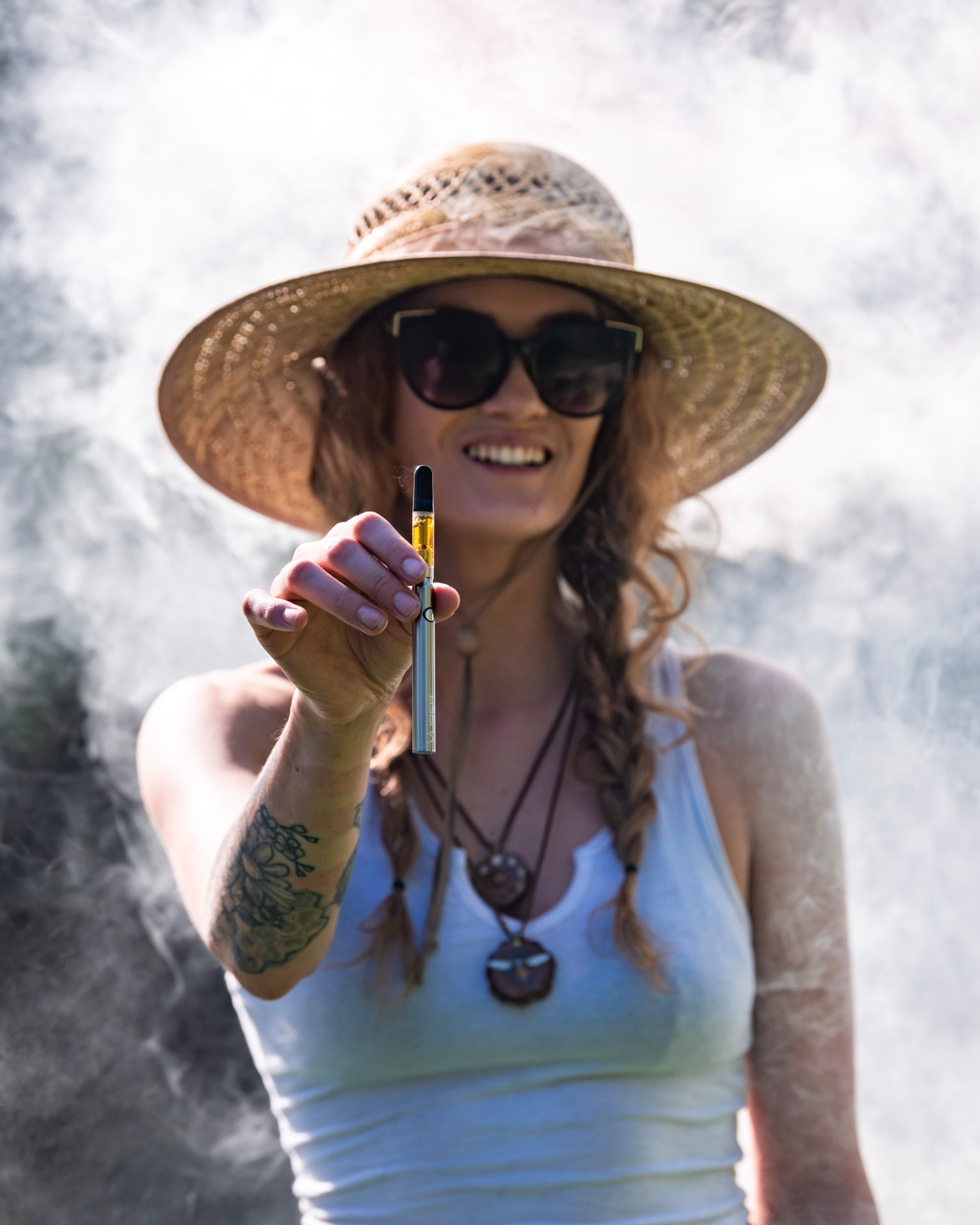 Woman in a straw hat holding up a Vuber slim battery in a cloud of vapor