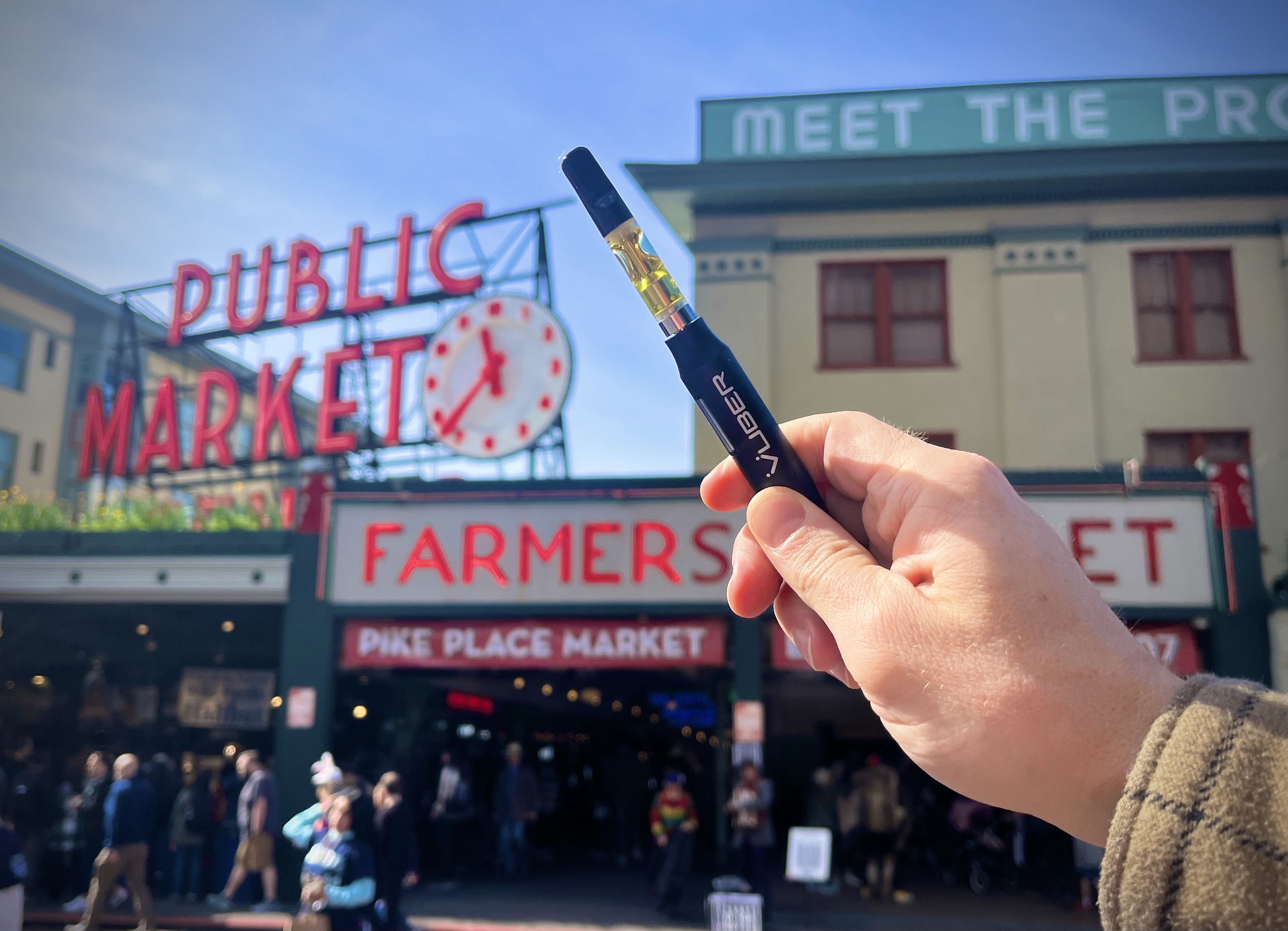 Hand holding a Vuber battery and quartz cartridge in front of the Pike Place Market sign in Seattle